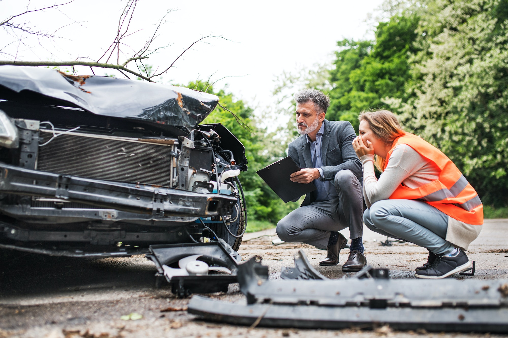 An insurance agent and a woman driver looking at the car on the road after an accident.